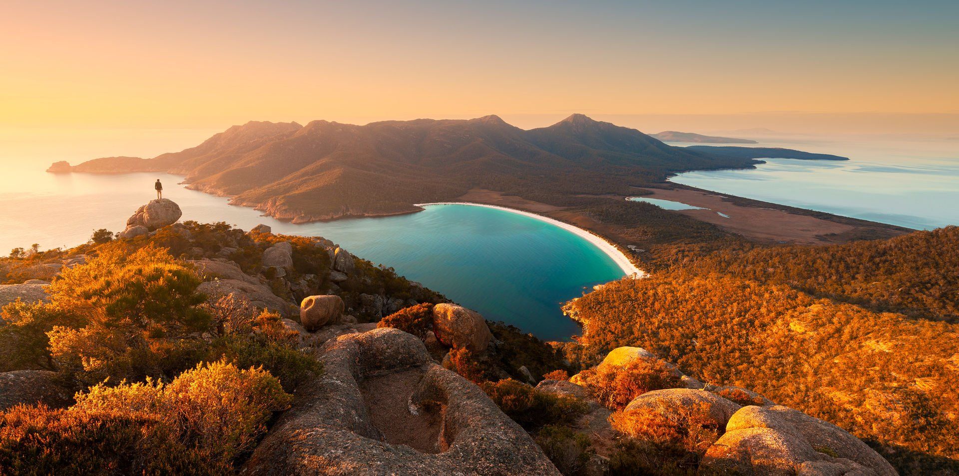 A person is standing on top of a mountain overlooking a body of water.
