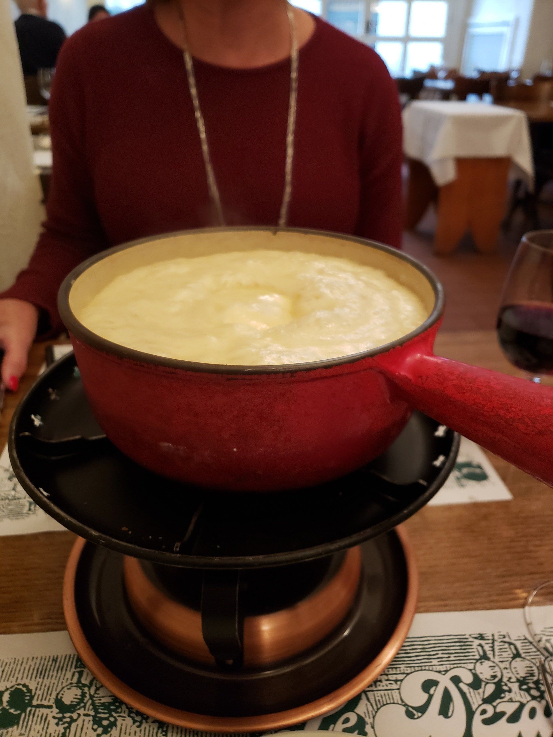 A woman is sitting at a table holding a bowl of fondue