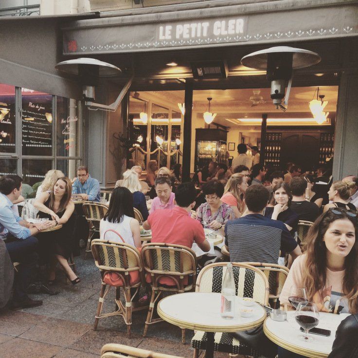 A group of people are sitting at tables outside of a restaurant called le petit cler