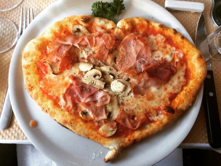 A heart shaped pizza with ham and mushrooms on a white plate.