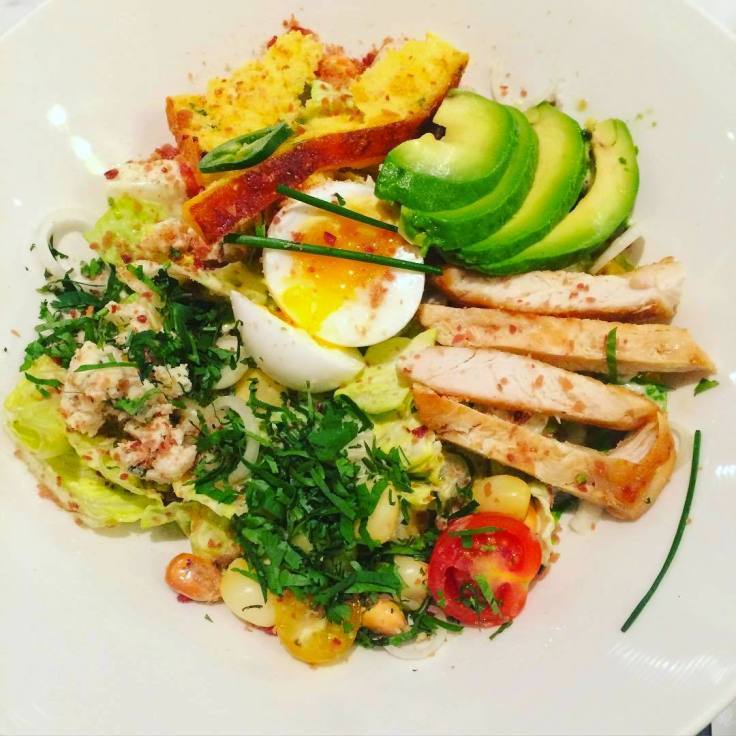 A salad with chicken , eggs , avocado and tomatoes on a white plate