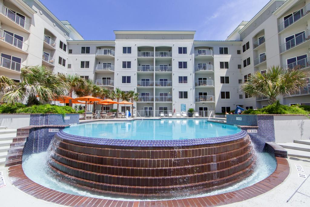 Pool in front of a multi-story, white building. Brick waterfall feature. Blue water and sky.