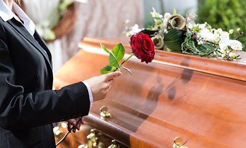 una donna con una rosa in mano e accanto una bara 