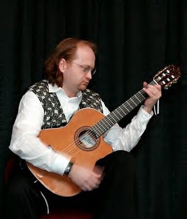 Man with long hair holding a guitar in a classical position