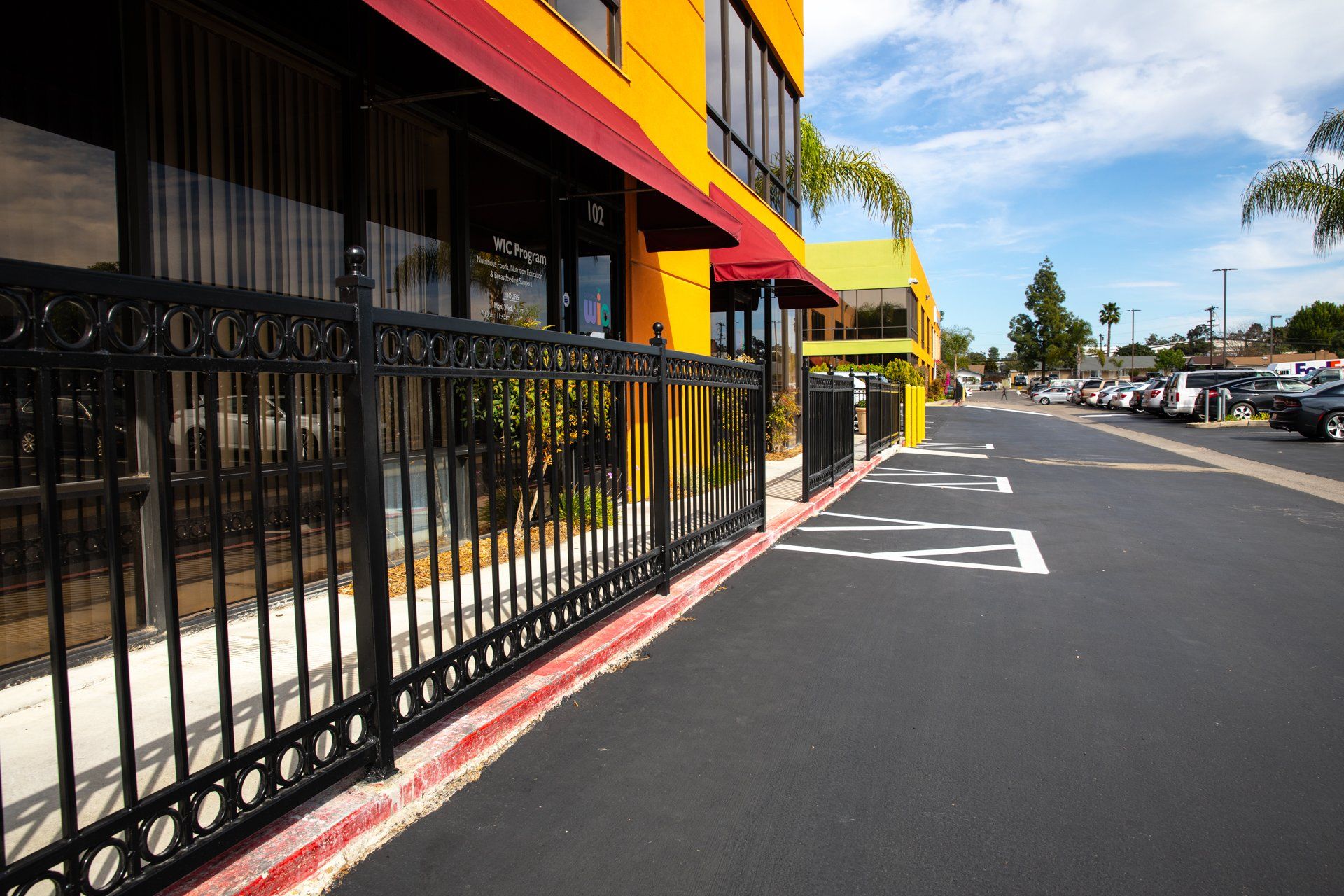 A yellow building with a red awning is behind a black fence