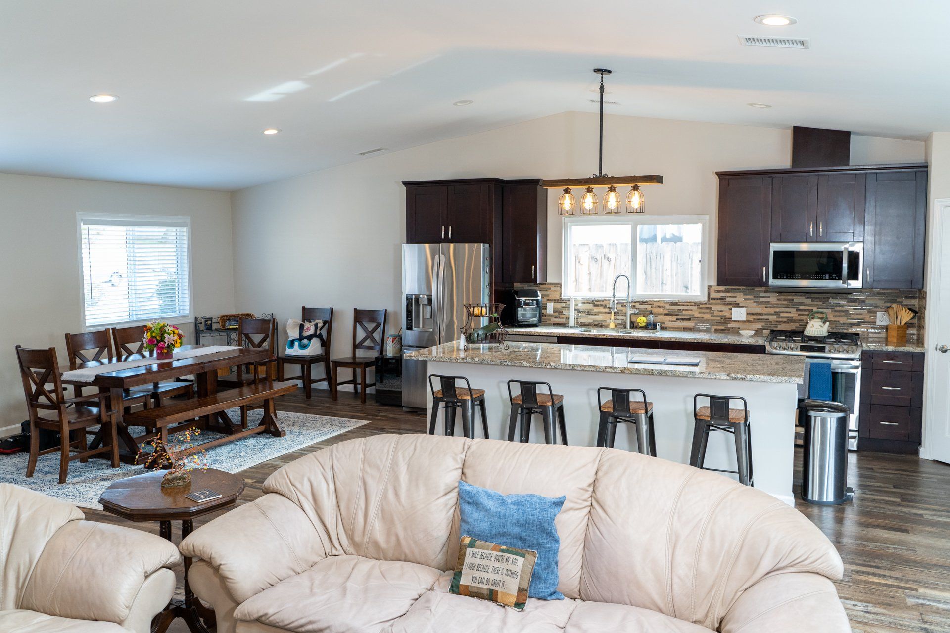 A living room with a couch , chairs , a table and a kitchen.