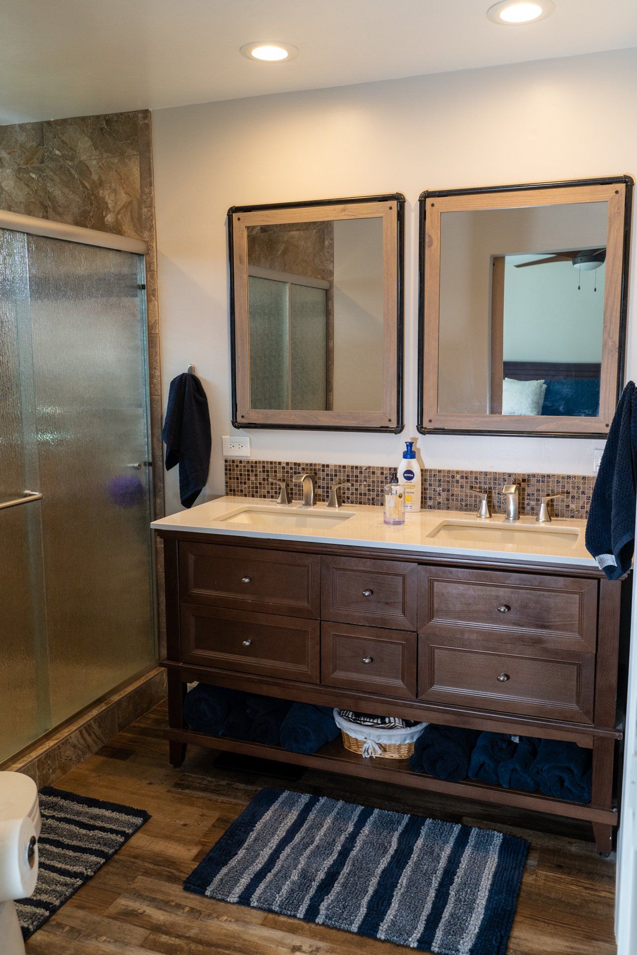 A bathroom with two sinks , two mirrors and a walk in shower.