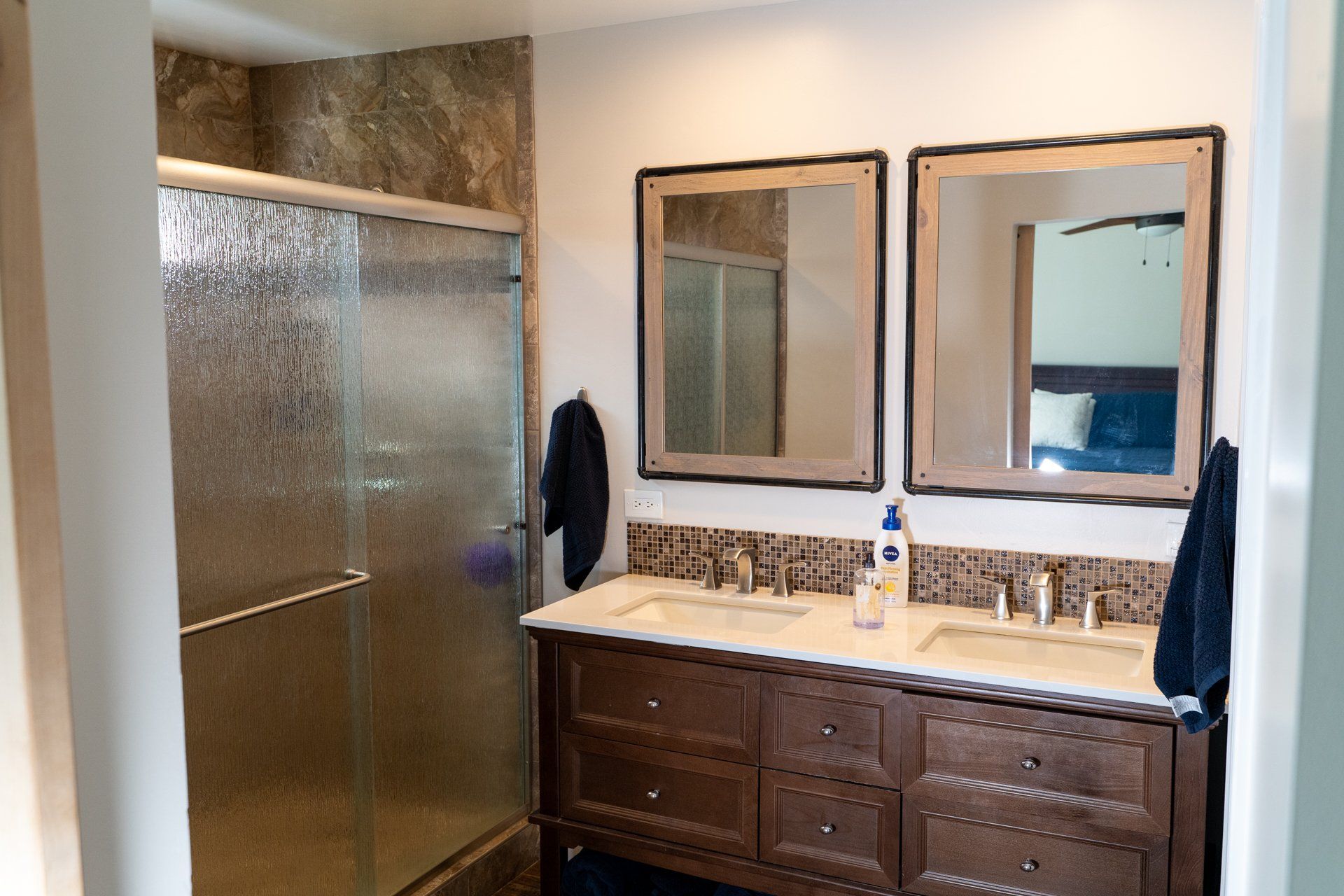 A bathroom with two sinks , two mirrors and a shower.