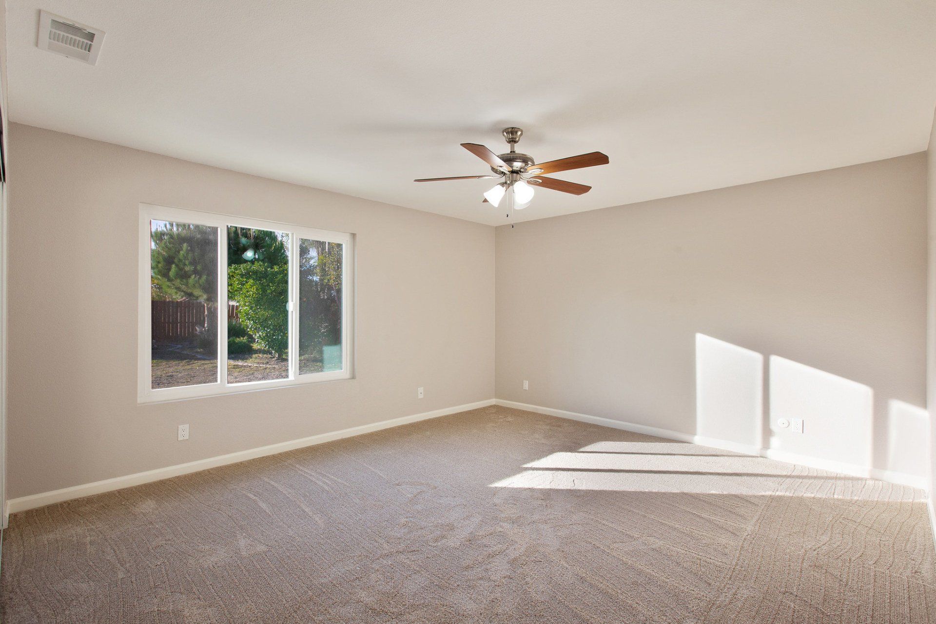 An empty room with a ceiling fan and two windows