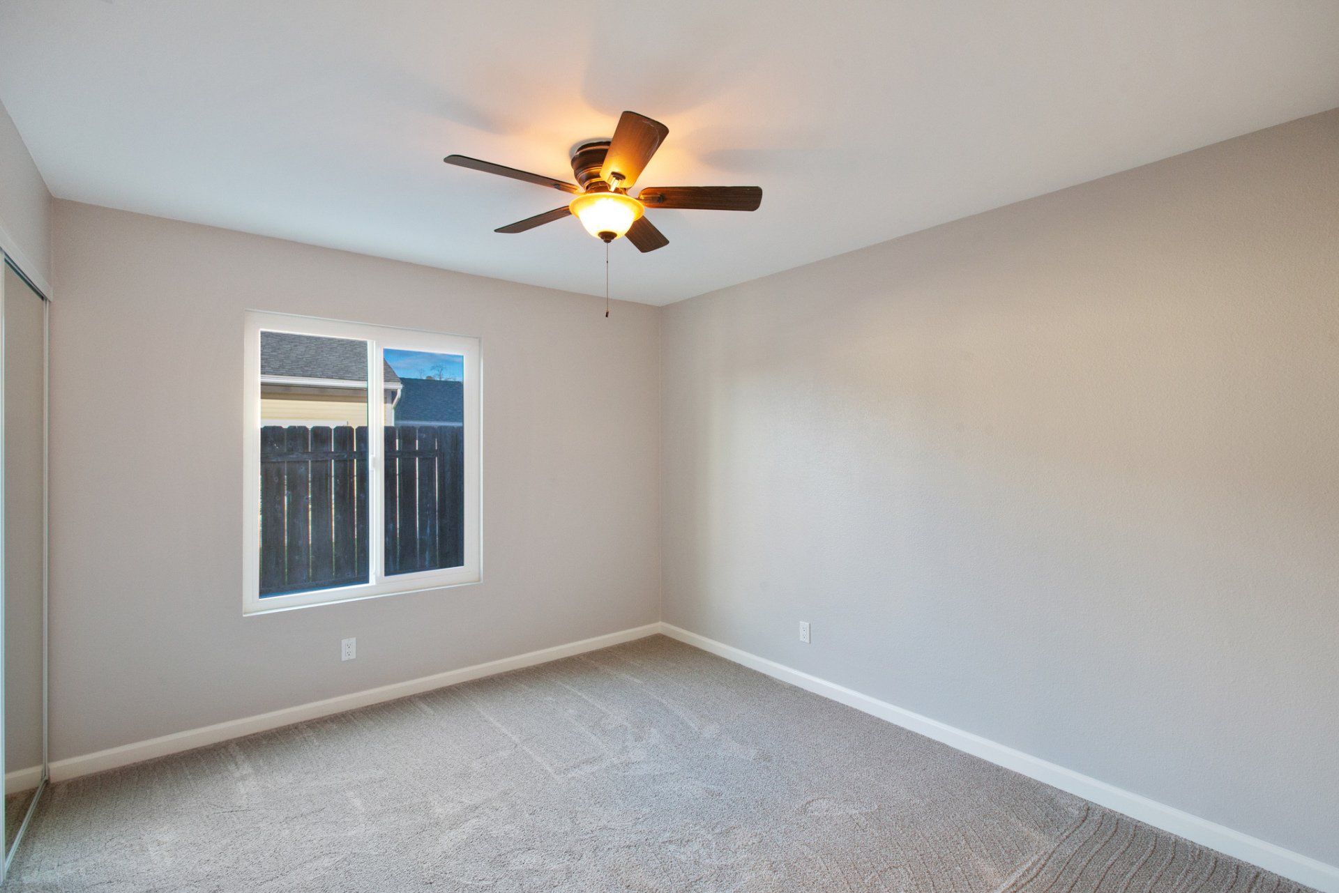 An empty bedroom with a ceiling fan and a window