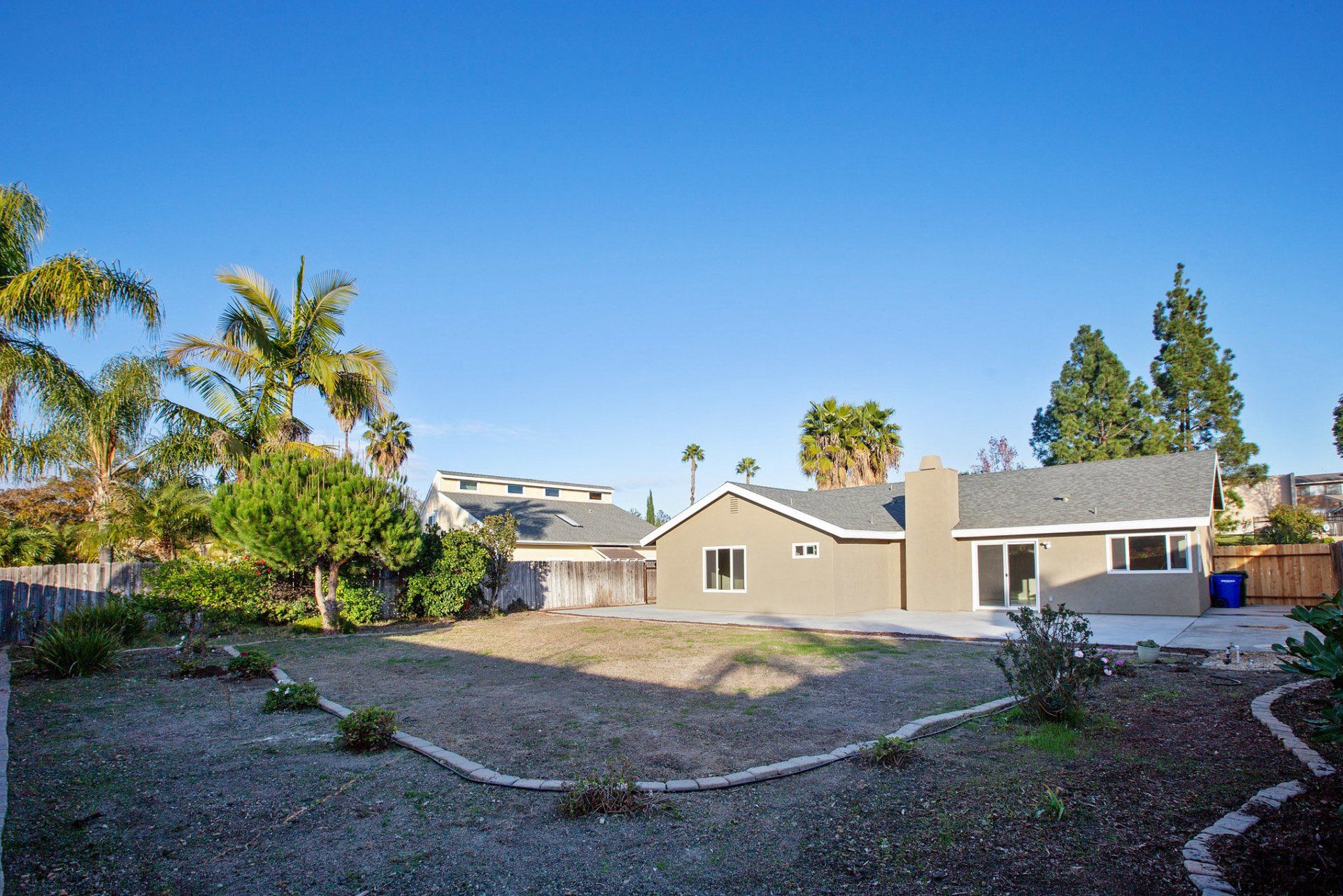A house with a gray roof is surrounded by palm trees