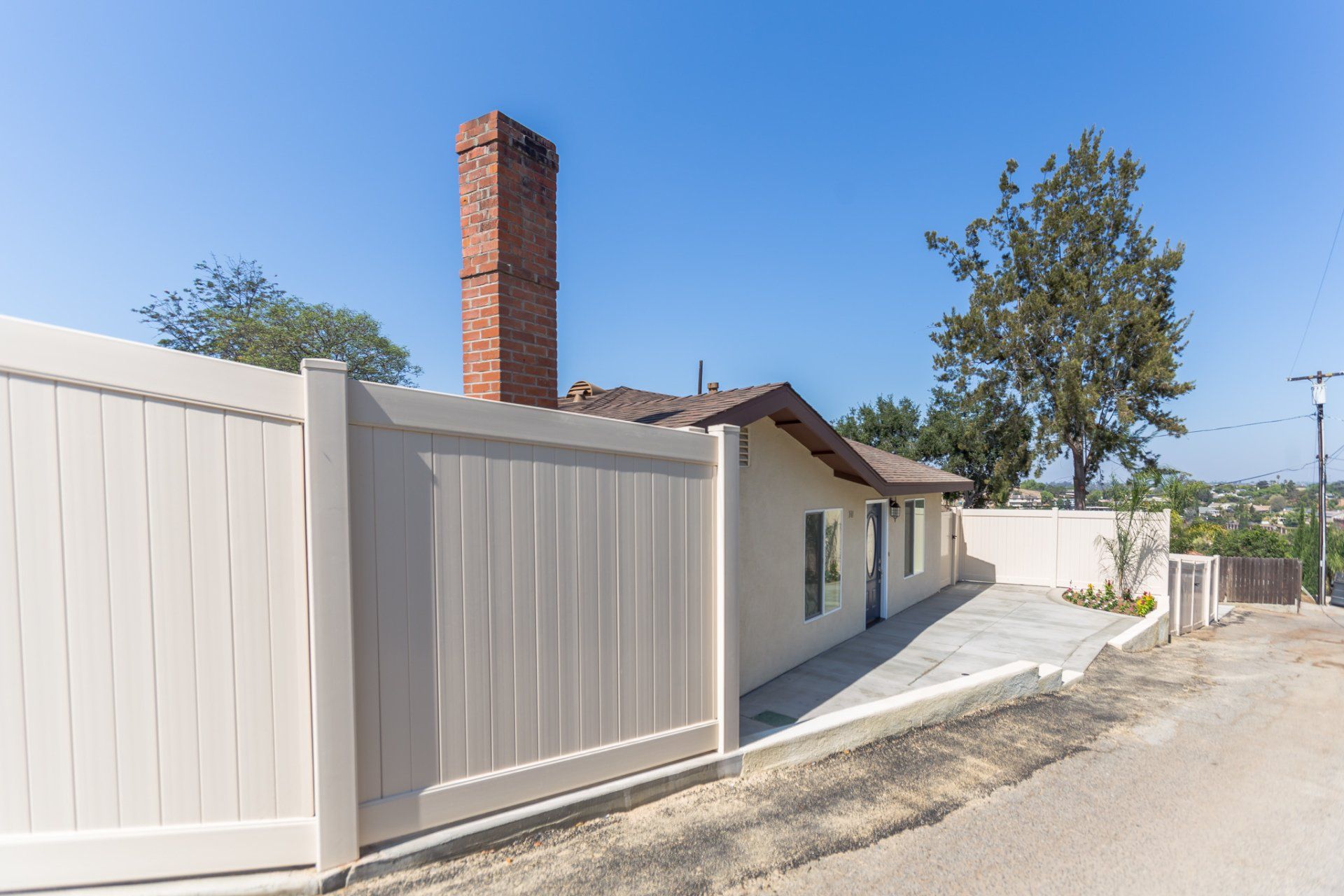 A white fence surrounds a house with a brick chimney in the background