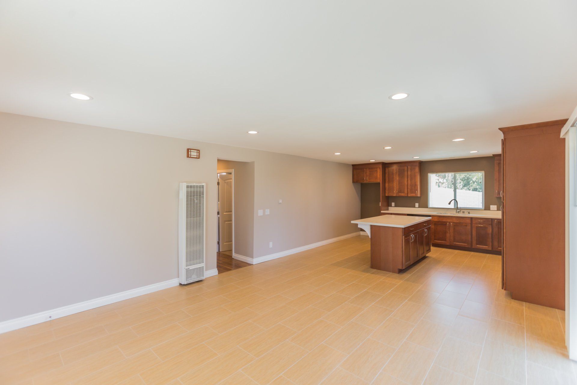 A large empty room with a kitchen in the background