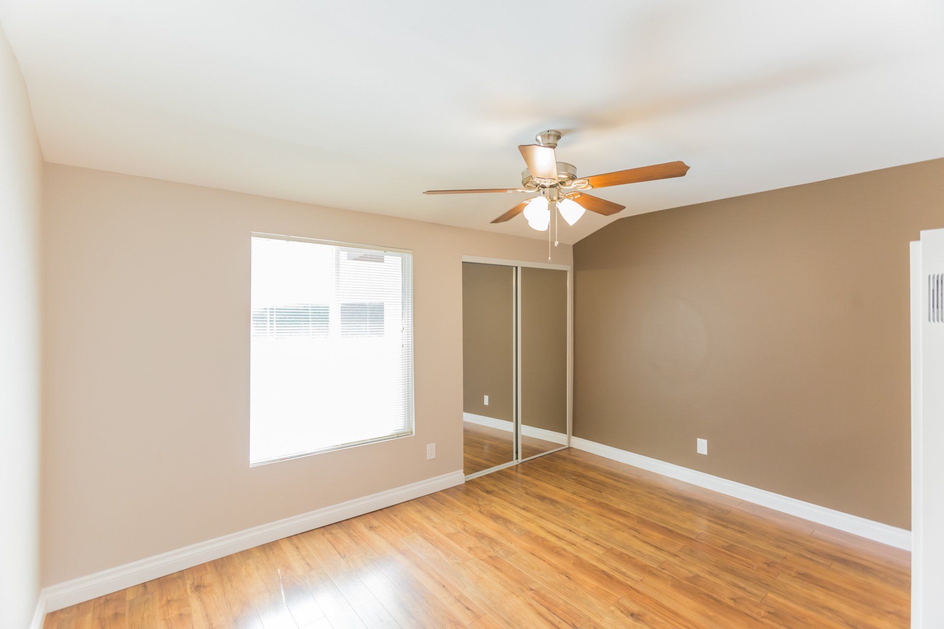 An empty bedroom with hardwood floors and a ceiling fan