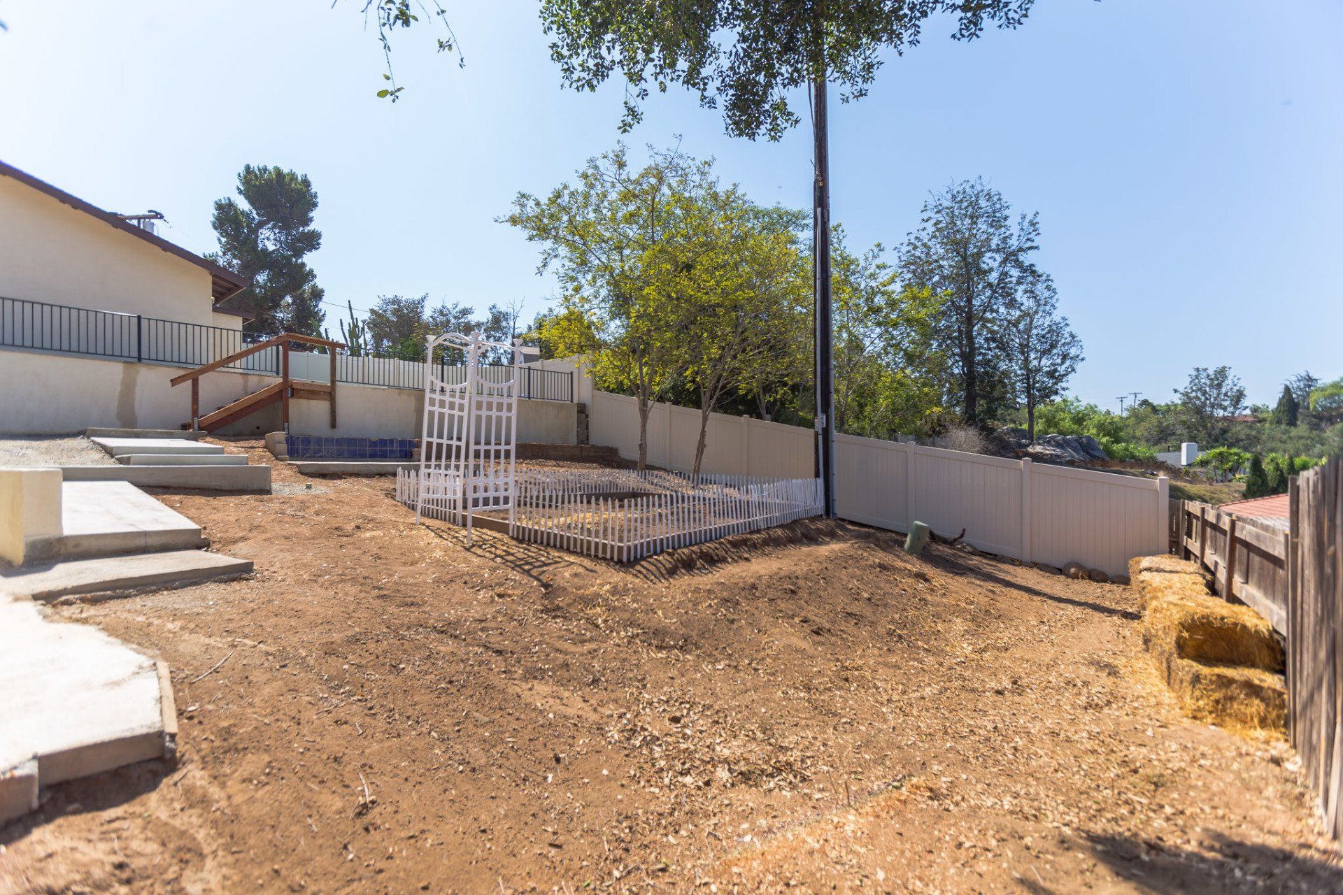 A dirt yard with a white fence and a tree