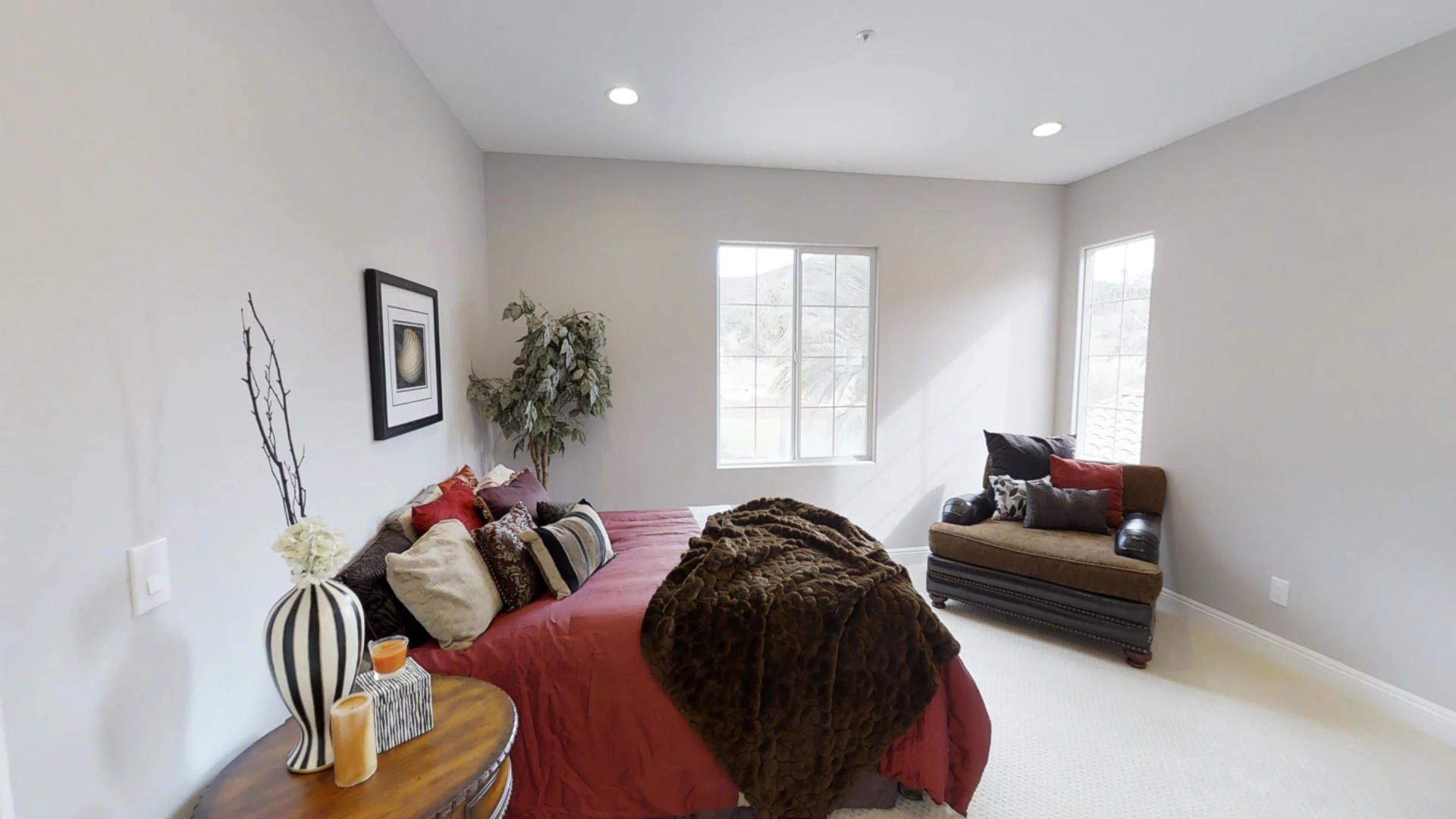 A bedroom with a bed , chair , nightstand and two windows.