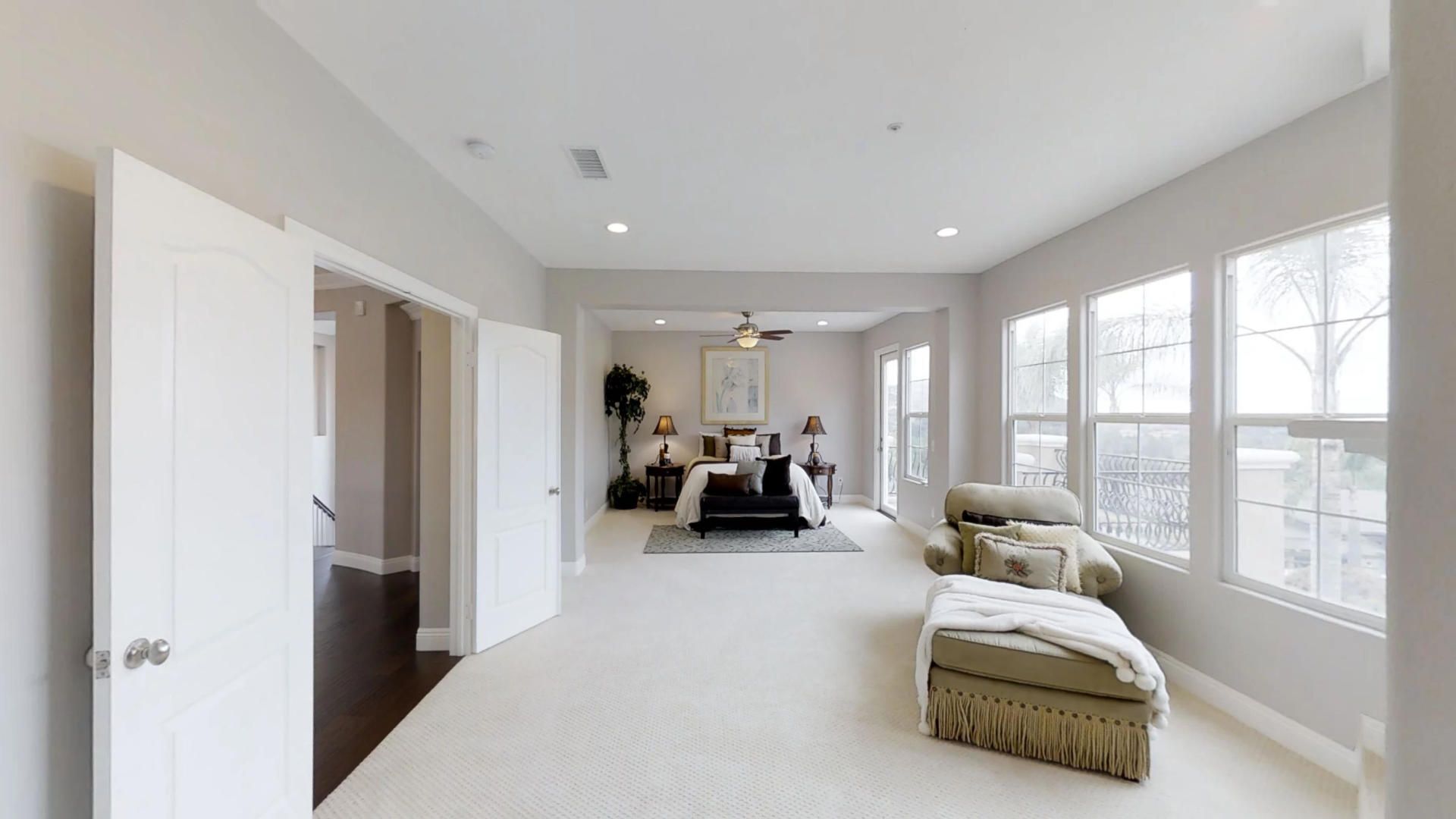 A large bedroom with a bed , chair , ottoman and lots of windows.