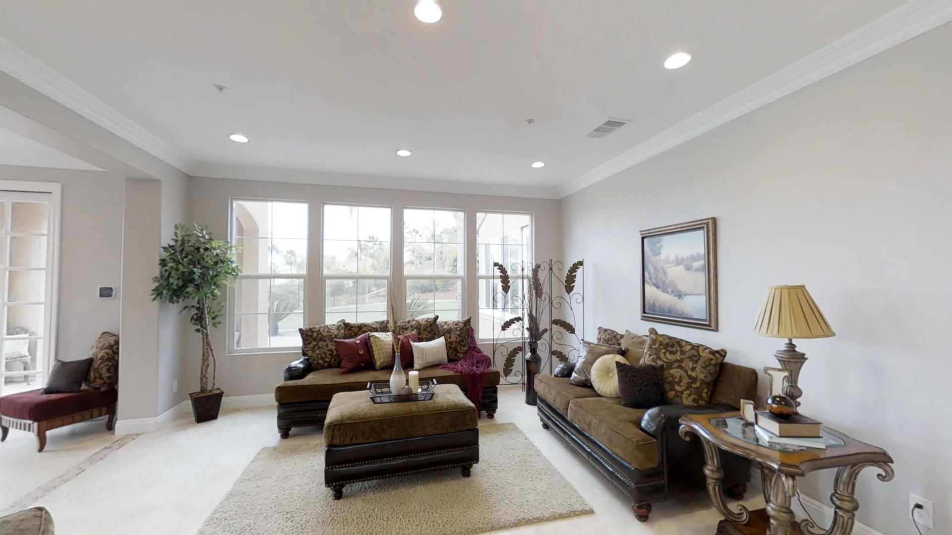 A living room with a couch , ottoman , table , chairs and a large window.