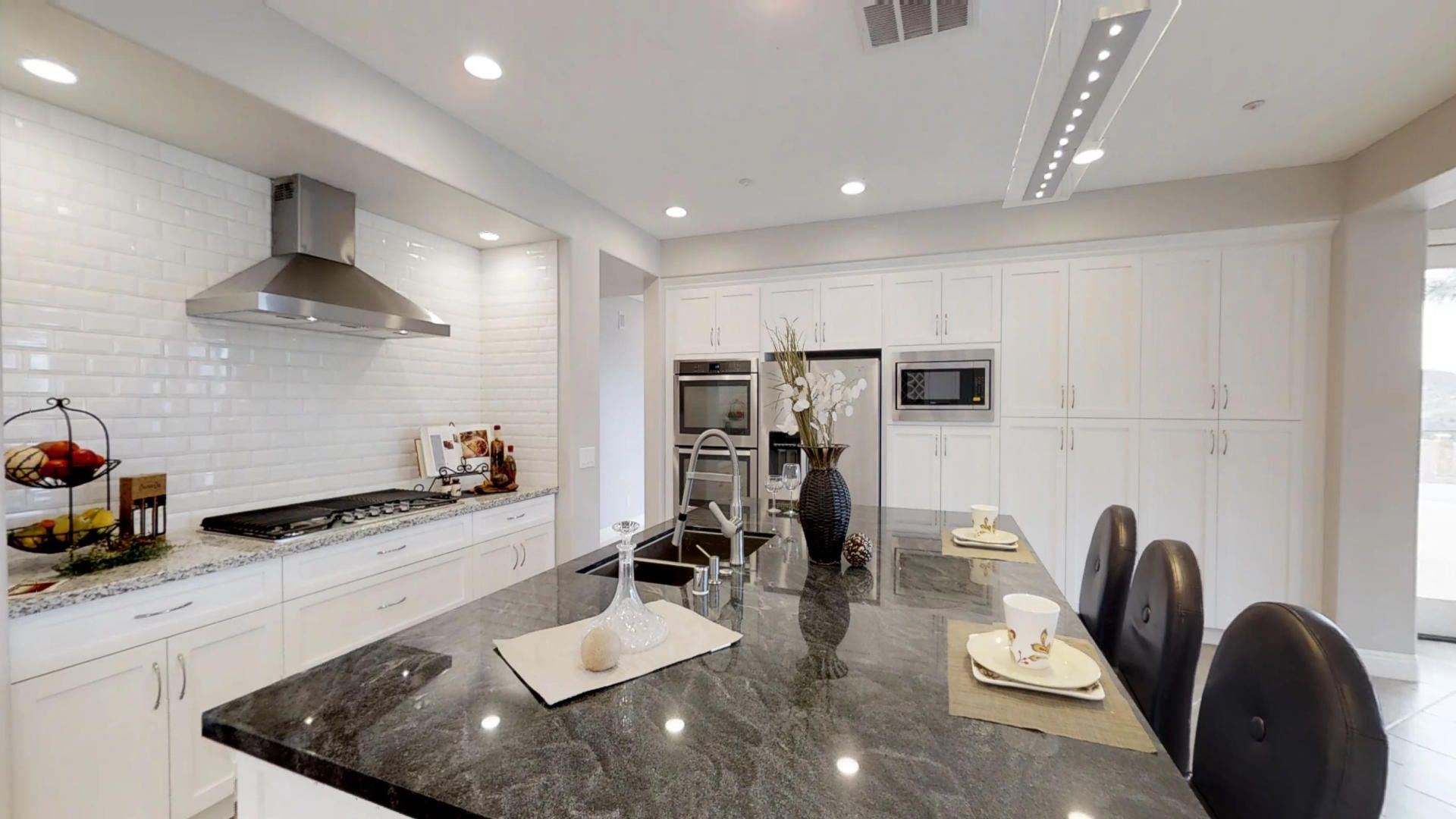 A kitchen with white cabinets , granite counter tops , stainless steel appliances and a large island.