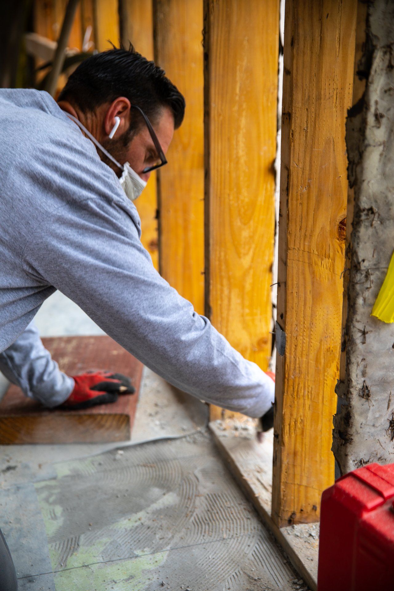 A man wearing a mask and gloves is cutting a piece of wood