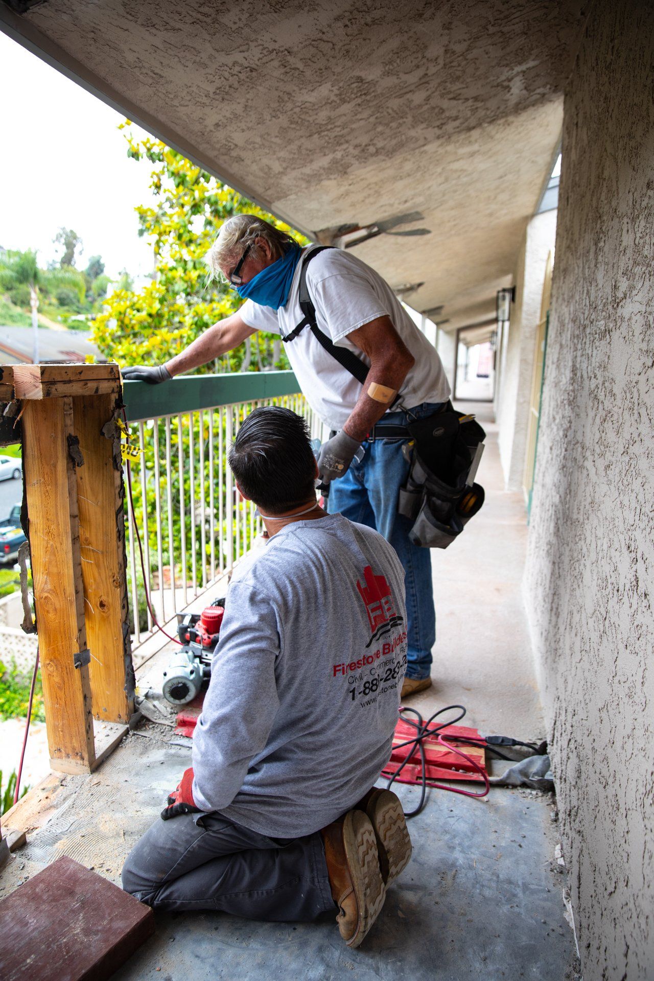 Two men are working on a balcony with one wearing a shirt that says ' abercrombie & fitch ' on the back