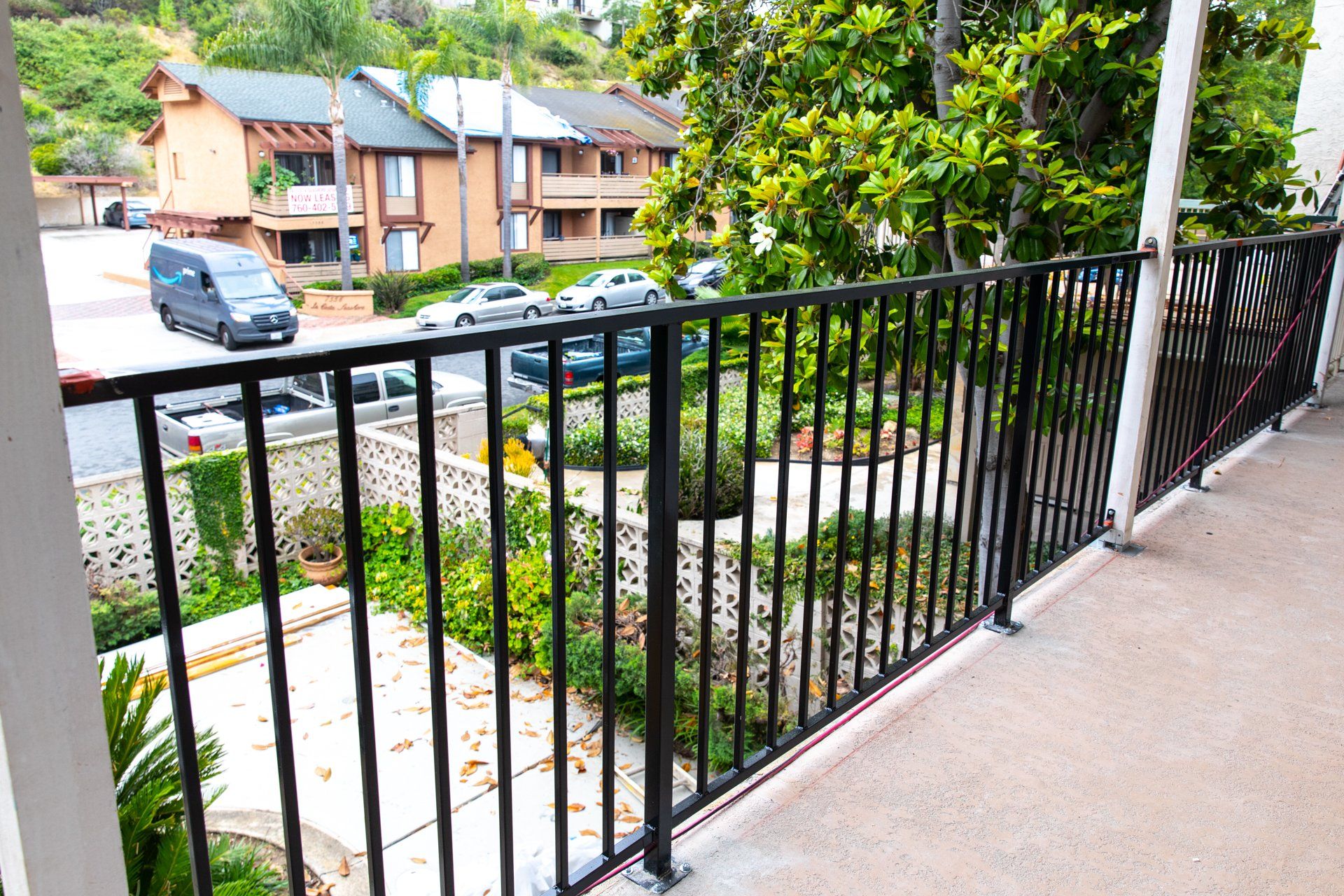 A balcony with a black railing overlooking a parking lot