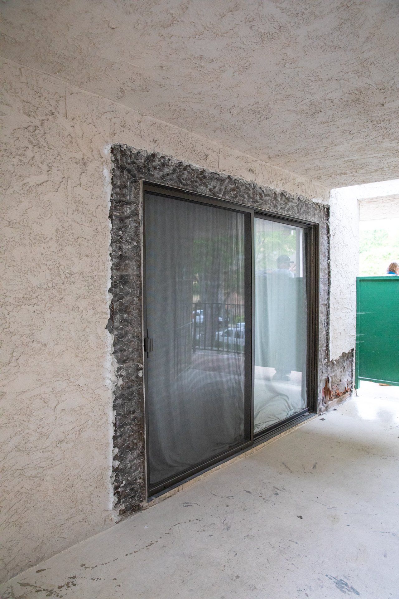 A sliding glass door with a green fence in the background