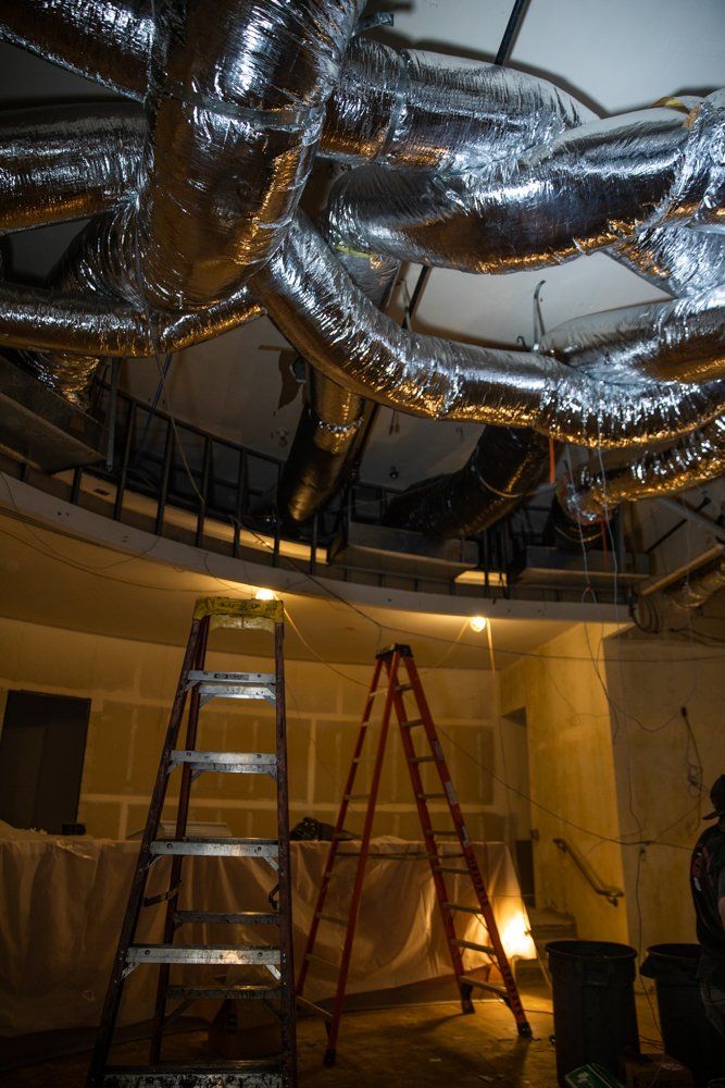 A room with a ladder and a bunch of pipes hanging from the ceiling.
