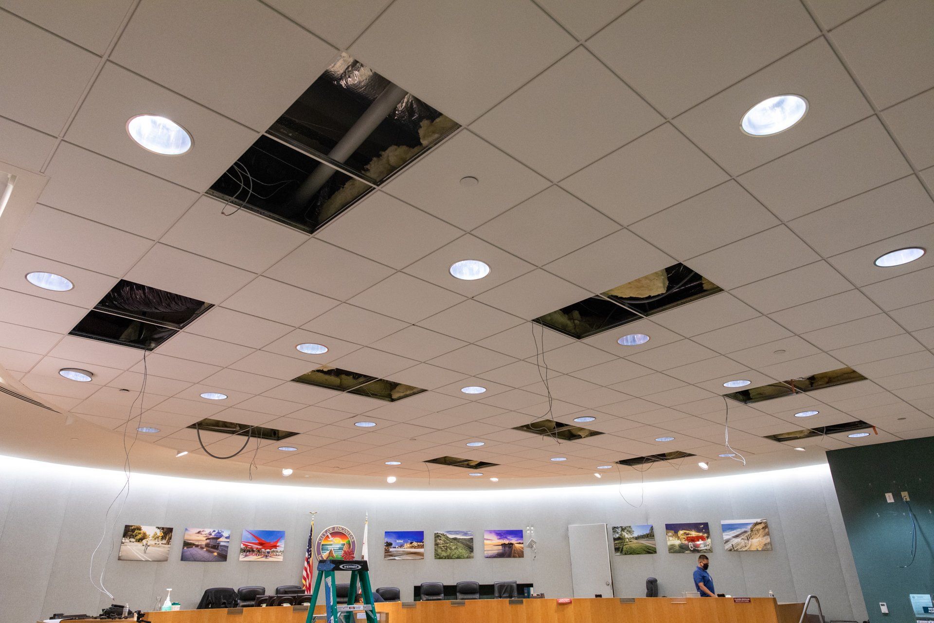 A man is standing on a ladder in a room with holes in the ceiling.