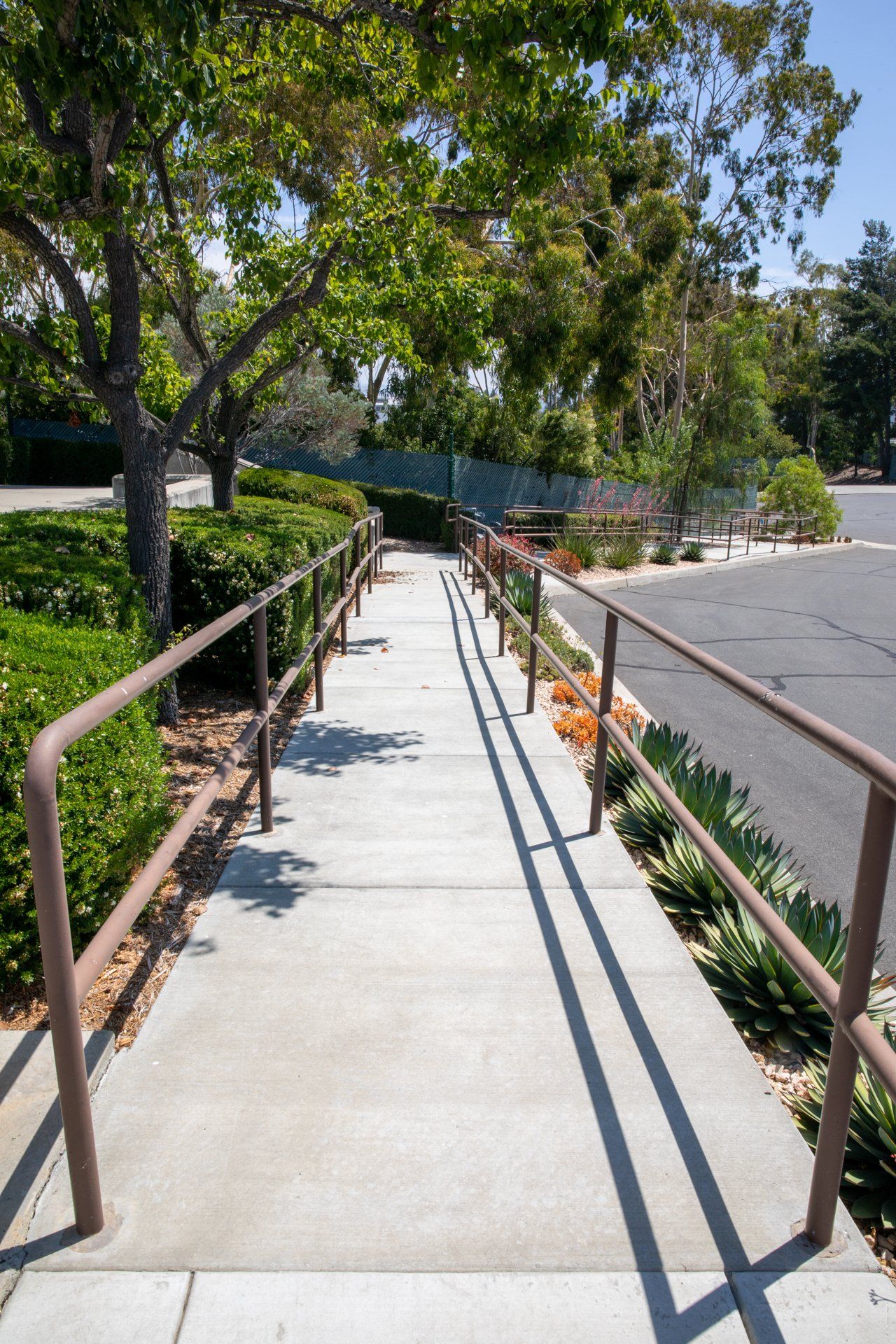 A concrete walkway with a metal railing leading to a parking lot.