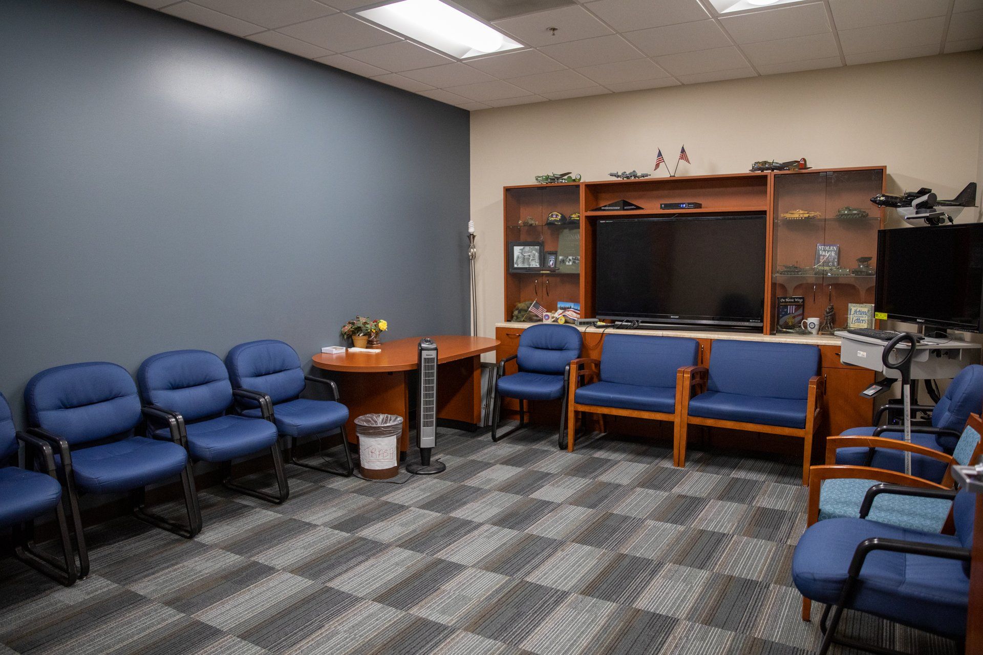 A waiting room with blue chairs and a flat screen tv.