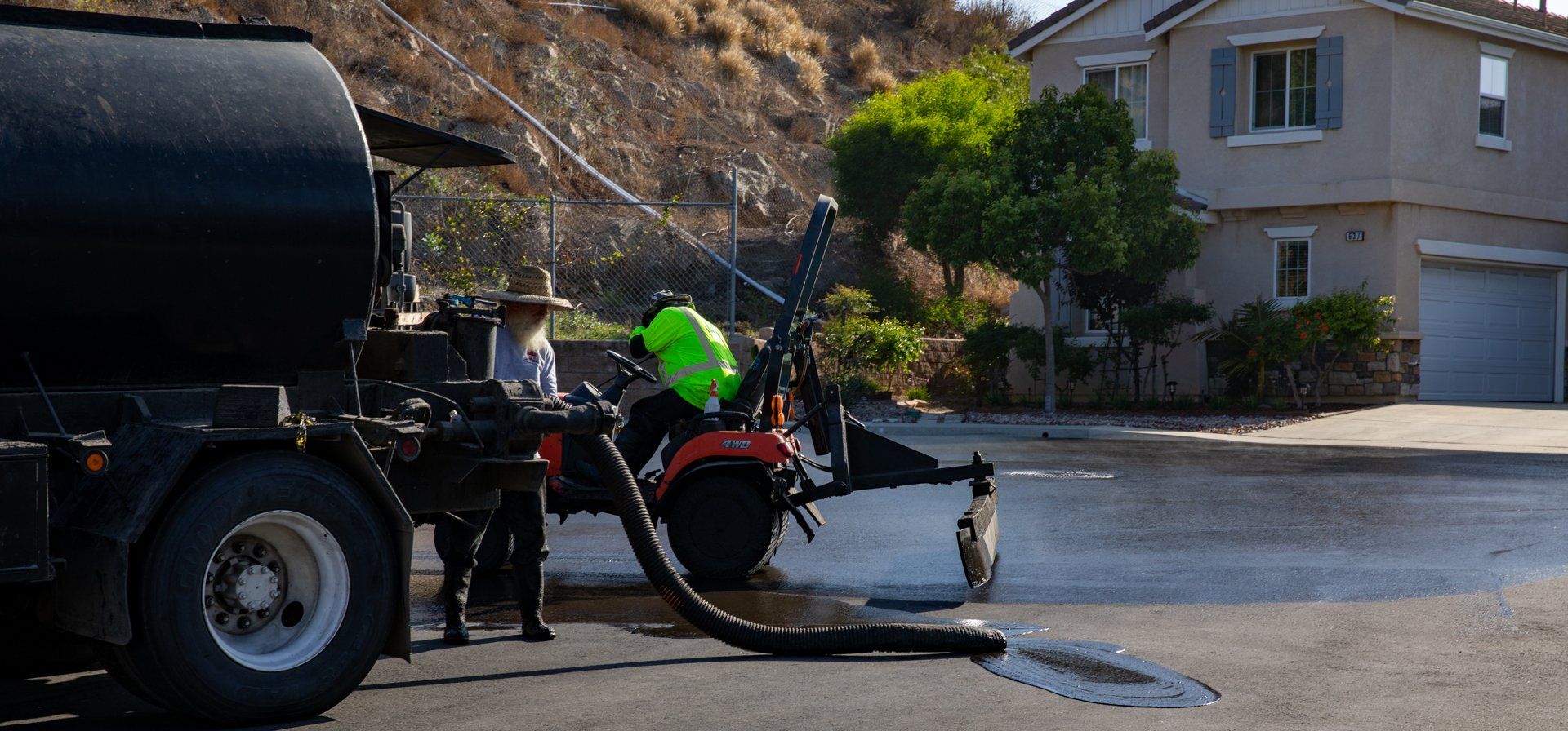 A man is spraying asphalt on a street in front of a house.