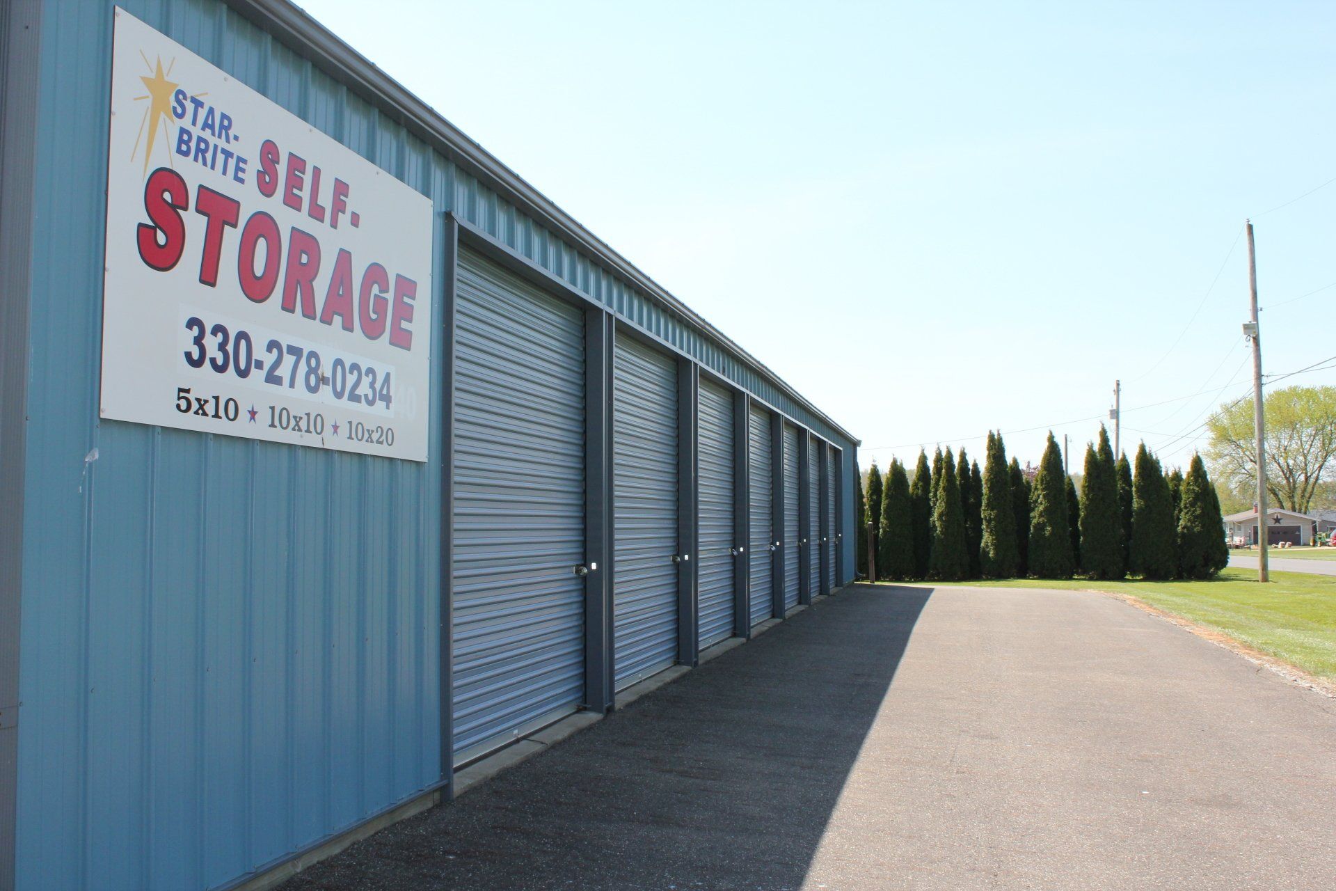 Blue Star-Brite Self Storage building with closed gray doors; sign with phone number.