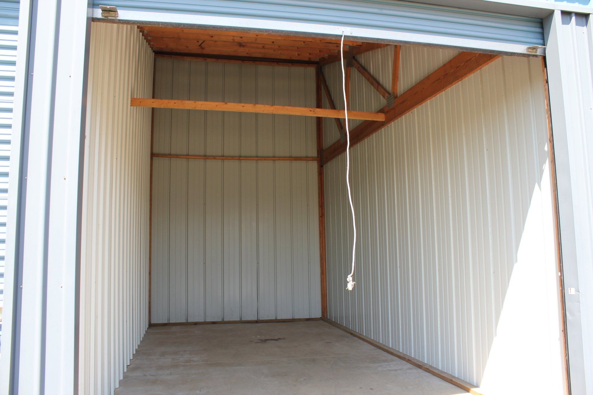 Empty storage unit with corrugated metal walls, concrete floor, and wooden beams.