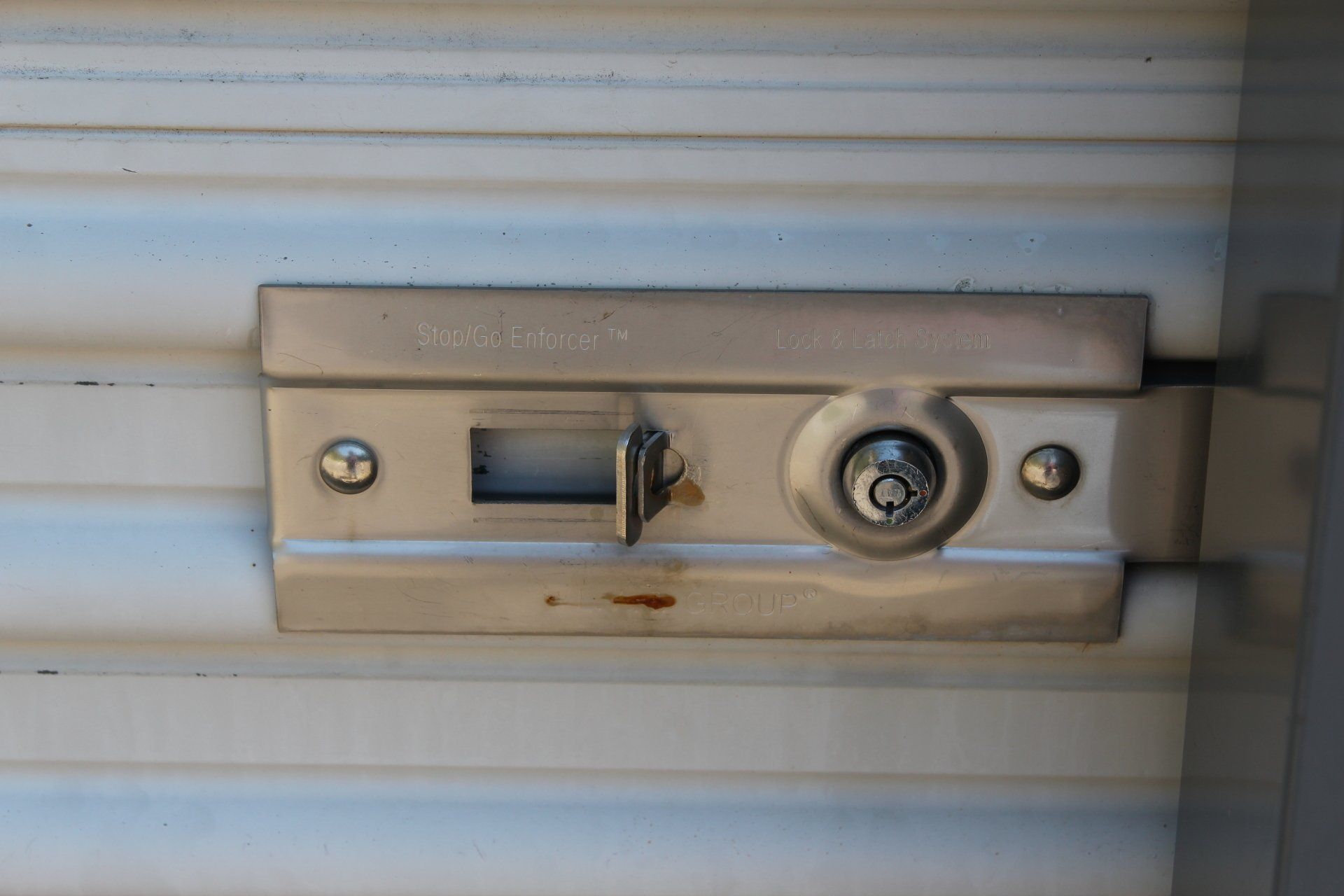Metal shed lock with keyhole and sliding latch on a corrugated surface.