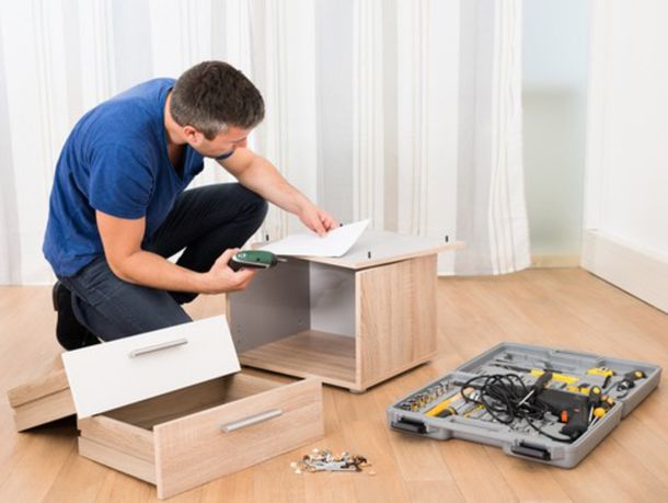 A man is kneeling down to assemble a nightstand in a living room.