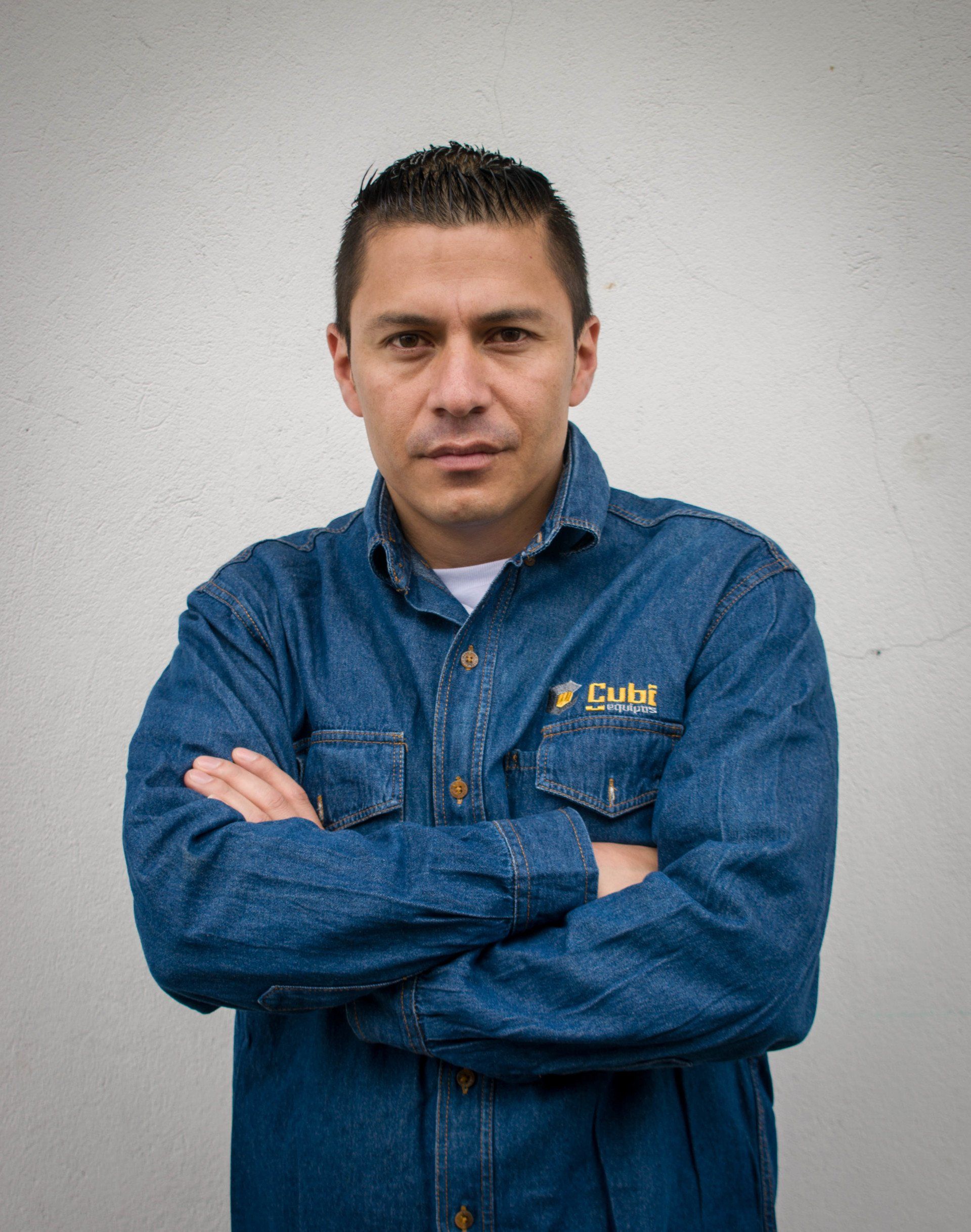 Un hombre con una camisa vaquera azul está de pie con los brazos cruzados.