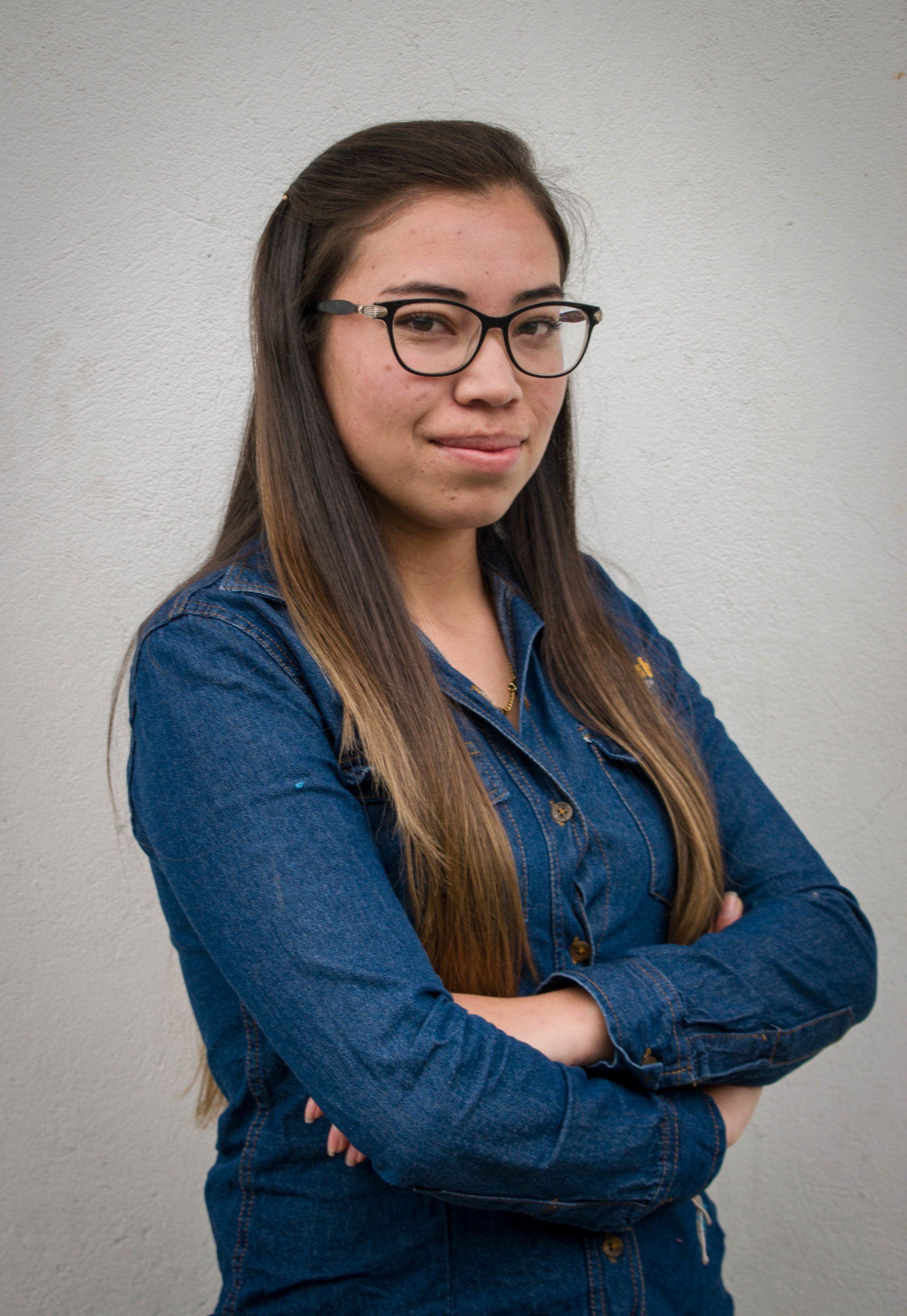 Una mujer que lleva gafas y una camisa azul está de pie con los brazos cruzados.