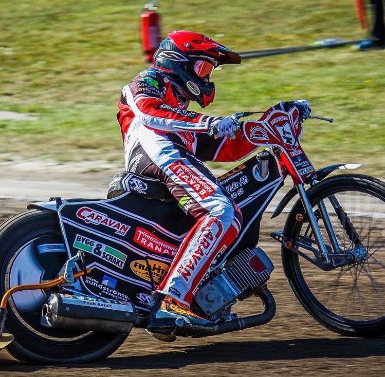 Speedway rider in red and white racing suit on a black and red motorcycle.