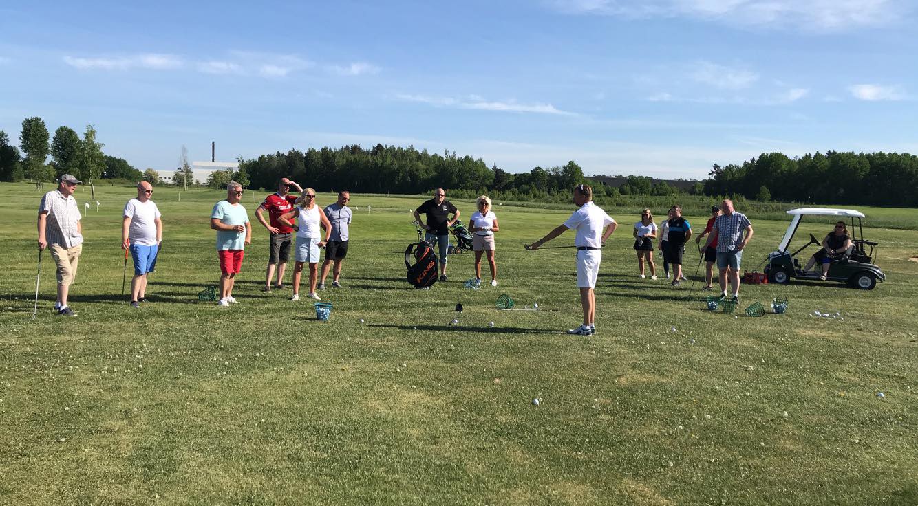 Group of people on a golf course watching a man demonstrate a golf swing.
