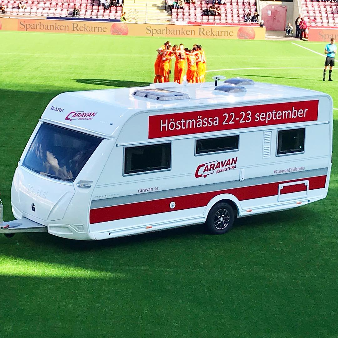 White caravan on a green field with red accents, advertisement for 