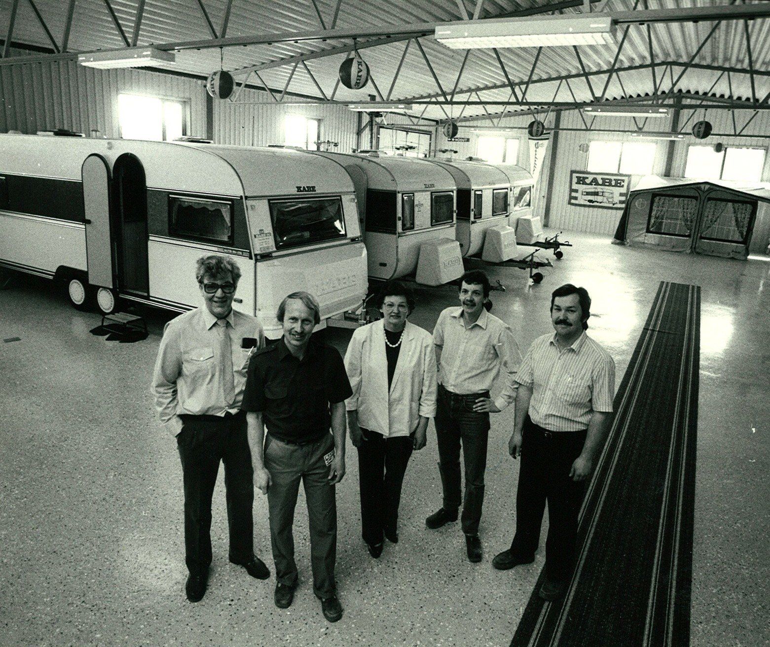 Five men stand in a large garage with several campers.
