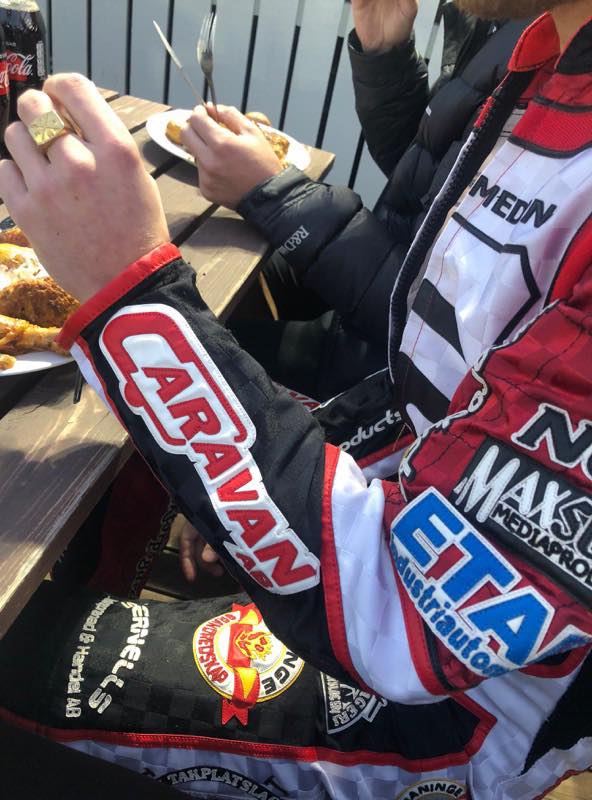 Man in racing jacket eats outdoors; 