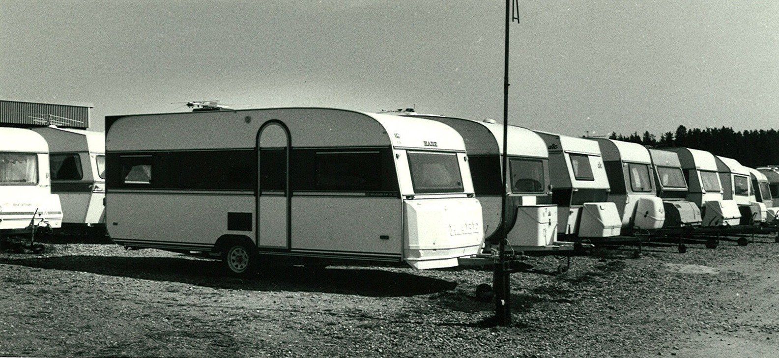 Row of white and striped camping trailers parked on a gravel lot under a clear sky.