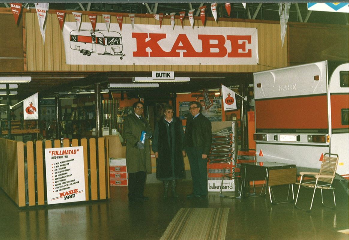 KABE caravan sales display with three people standing in front. Red and white signage and caravans visible.