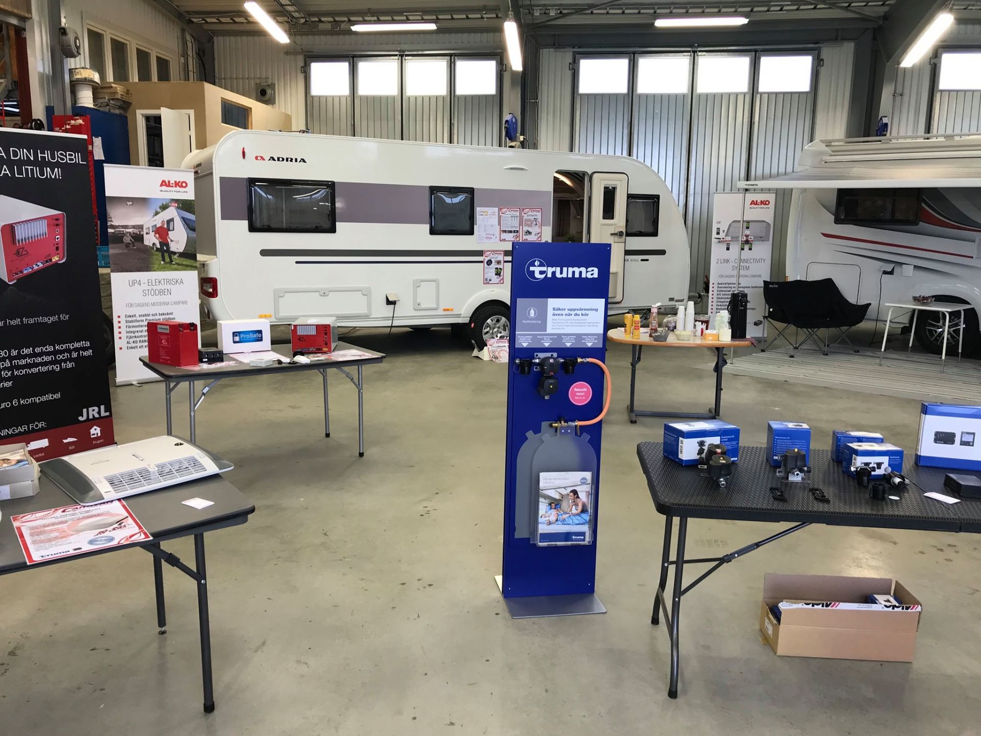 Inside a workshop, caravans on display with tables of equipment and information stands.