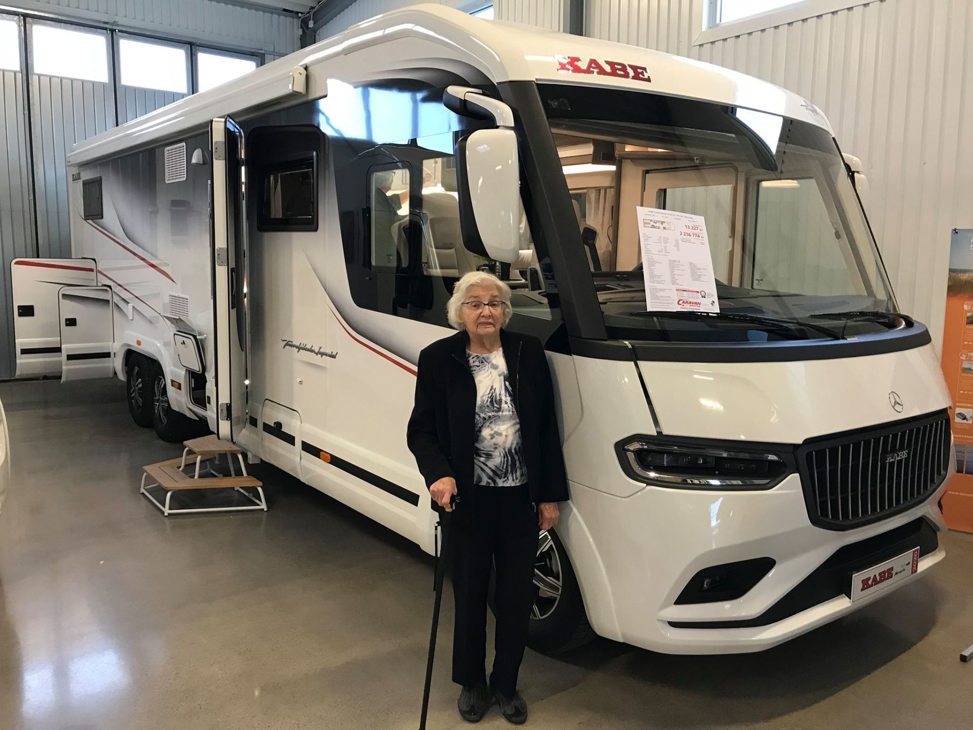 An elderly person with a cane stands next to a white motorhome with a large open door.