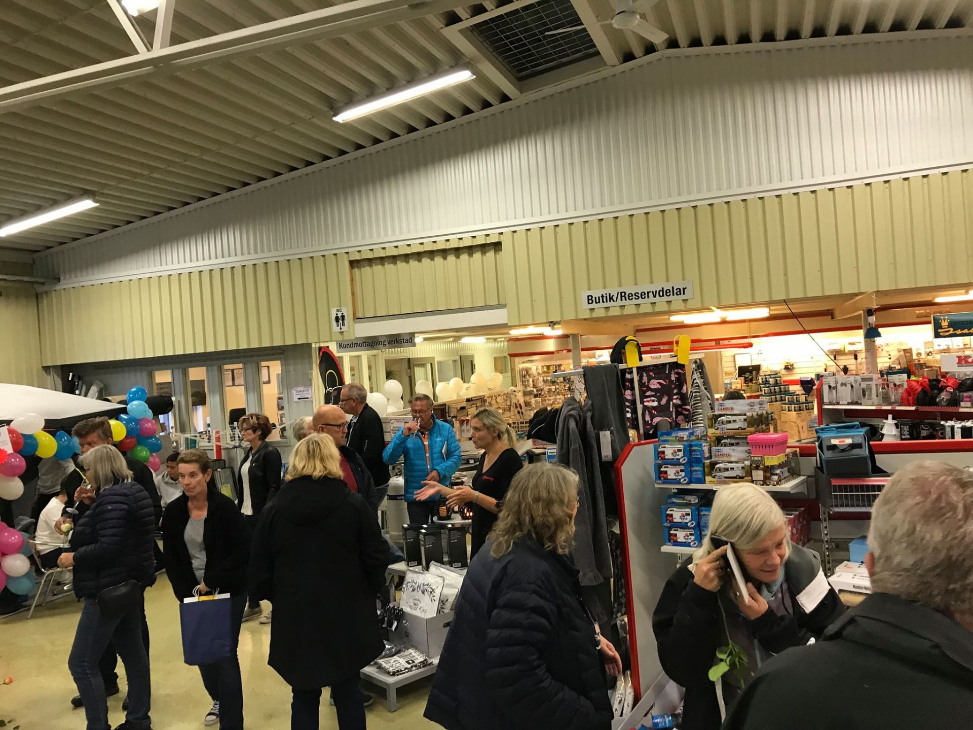People shopping in a store; balloons, products on display, doorway, light-colored walls and ceiling.