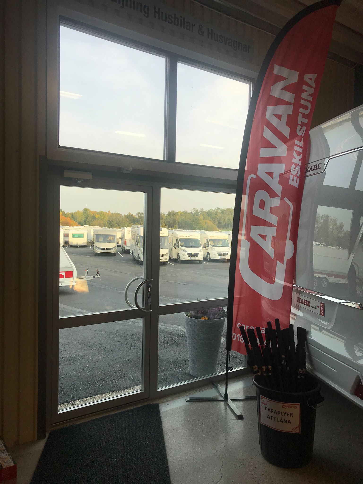 View from inside, through a glass door, of RVs parked outdoors; a flag reads