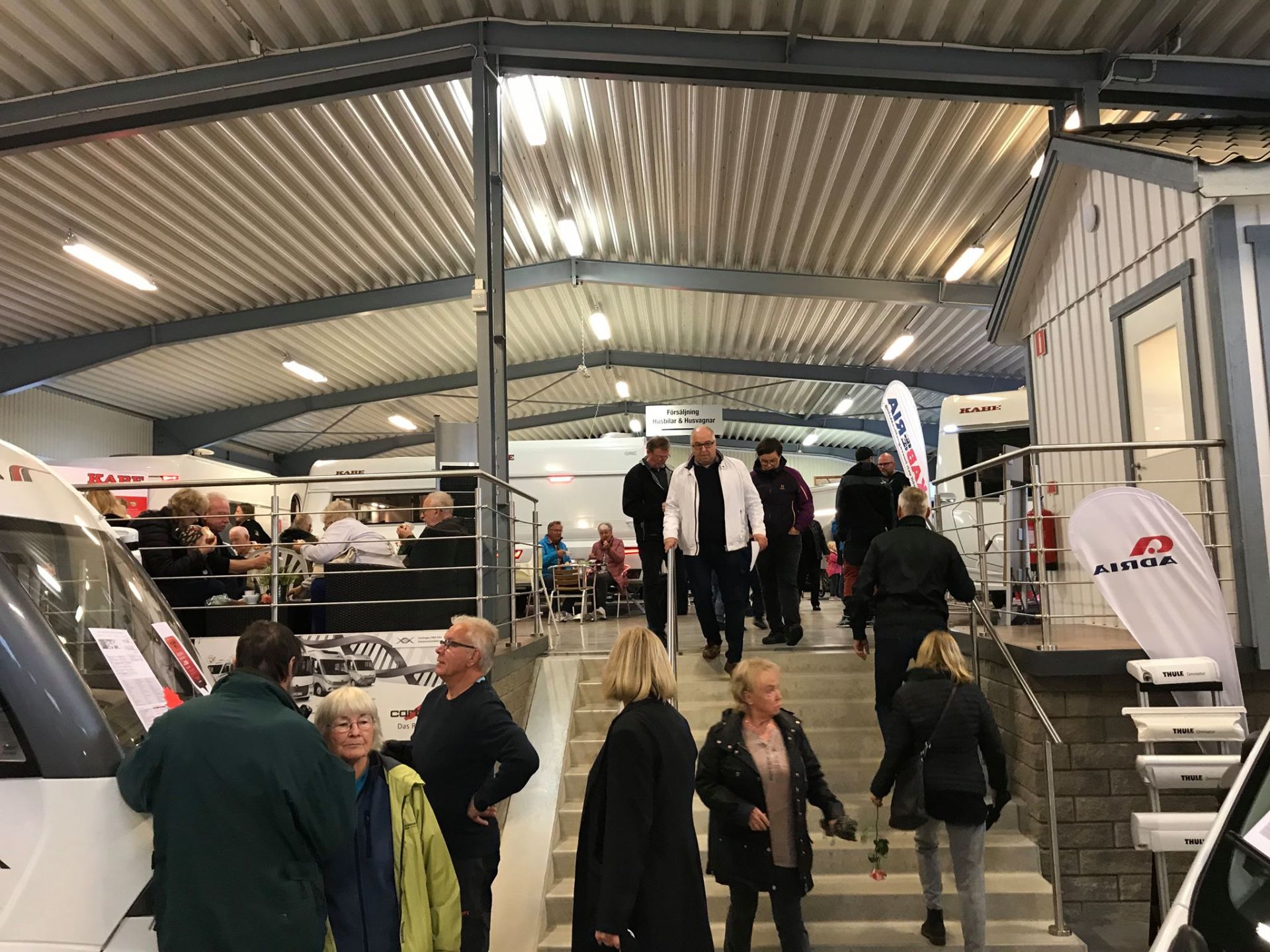 People walk up and down interior stairs at a trade show with RVs and booths.